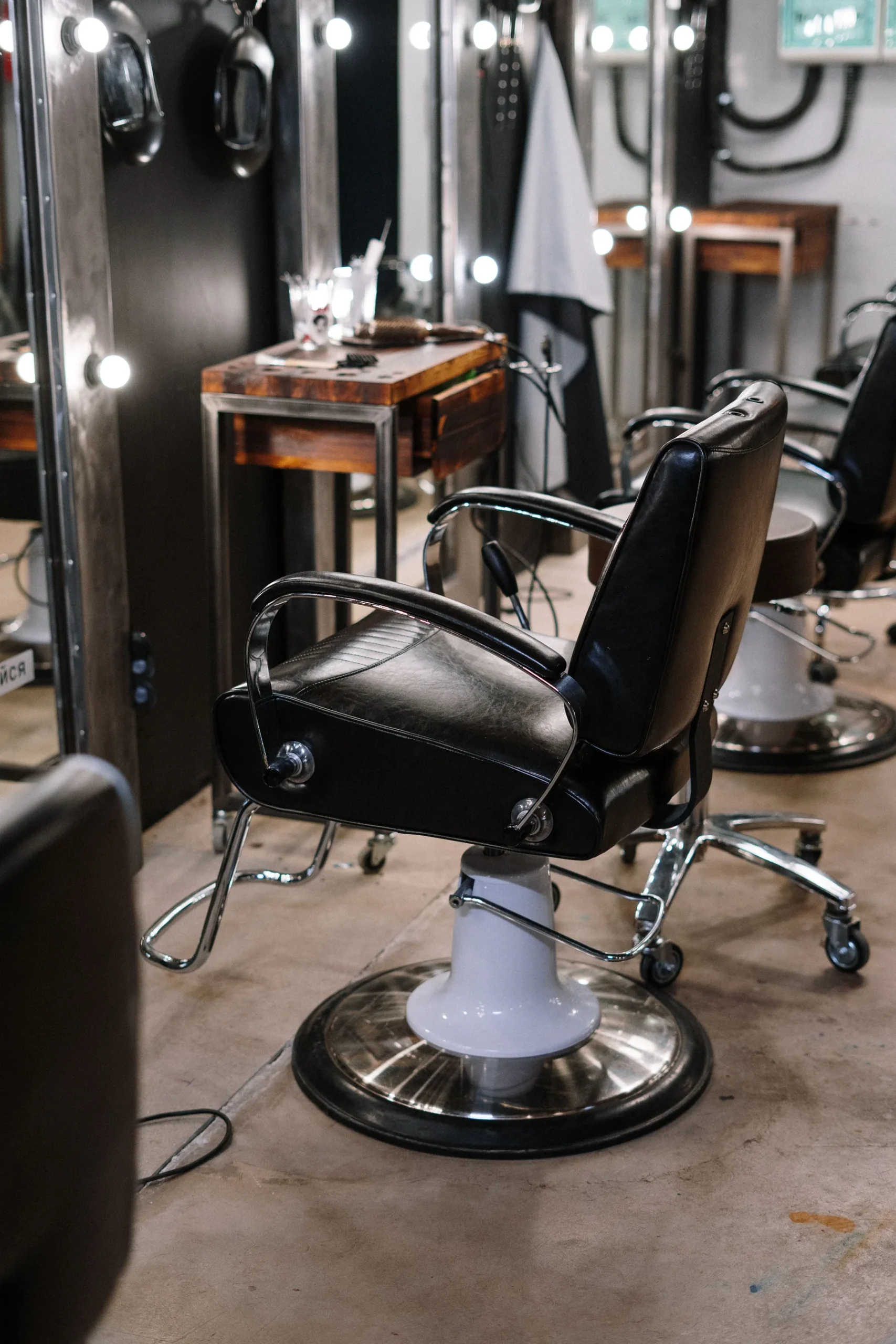 An empty dark styling chair in front of an illuminated mirror; editorial salon-context photograph