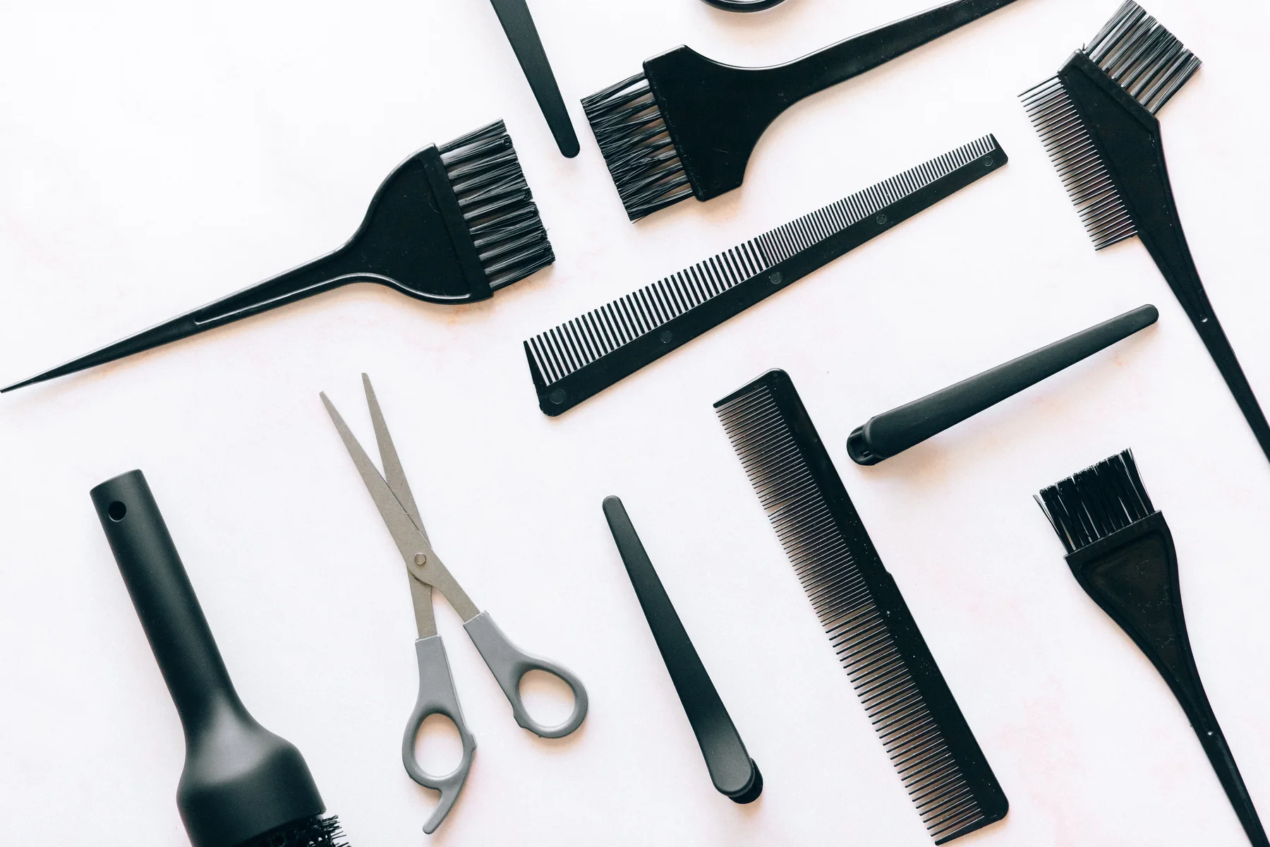 Hairbrushes, combs, clips and scissors arranged on a light surface; editorial tools photograph